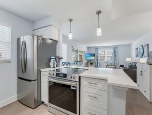 A modern kitchen with a built-in oven, a refrigerator, and a dining area with a view. - El Mar Condos #113 - "three Sisters" (North Redington Beach)