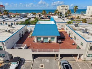 A multi-story building with a blue roof, outdoor seating area, and a parking lot. - El Mar Condos #113 - "three Sisters" (North Redington Beach)