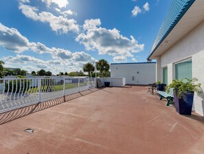 An outdoor patio area with a white fence, a bench, and a building with a blue roof. - El Mar Condos #113 - "three Sisters" (North Redington Beach)
