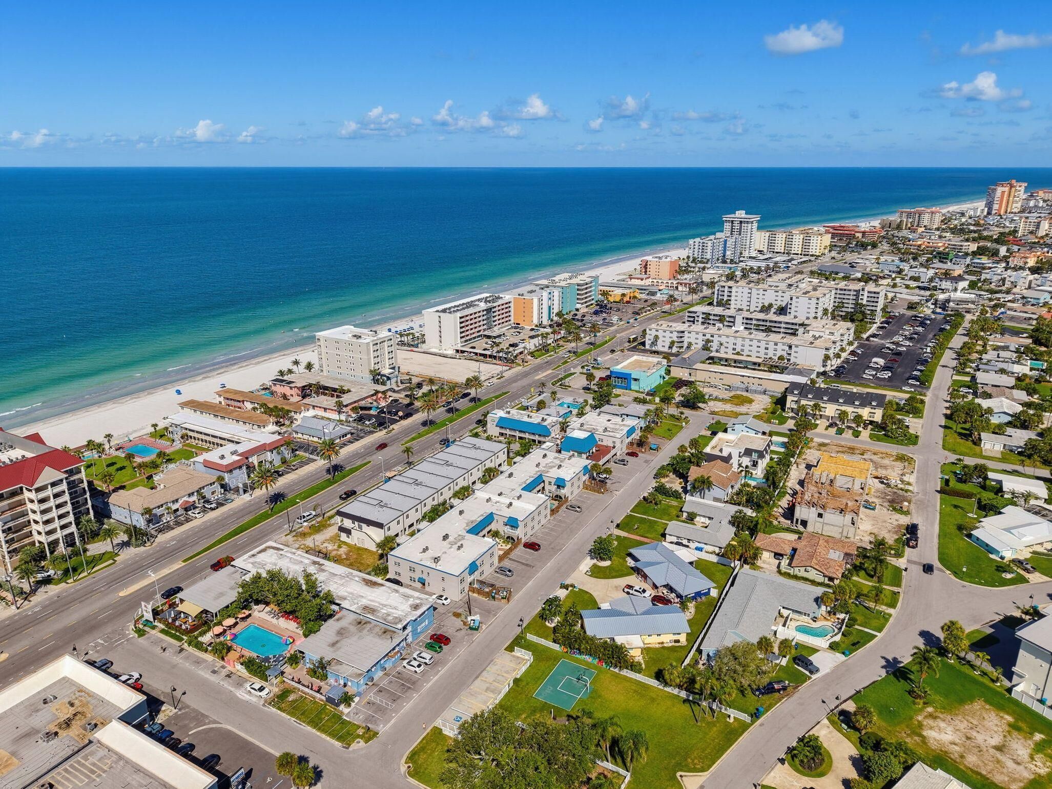 Ein Luftbild einer Küstenstadt mit Strand, Gebäuden, Straßen und blauem Himmel.