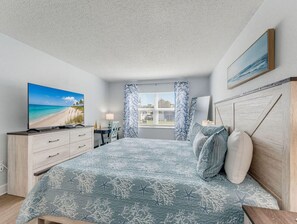 A bedroom with a bed, a TV, a desk, and a window with curtains. - El Mar Condos #113 - "three Sisters" (North Redington Beach)