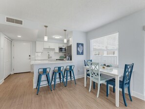 A modern kitchen with white cabinets, a central island, and blue bar stools. - El Mar Condos #113 - "three Sisters" (North Redington Beach)