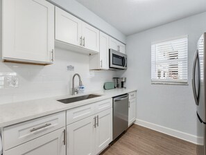Een moderne keuken met witte kasten, roestvrijstalen apparatuur, een magnetron en een raam met jaloezieën.