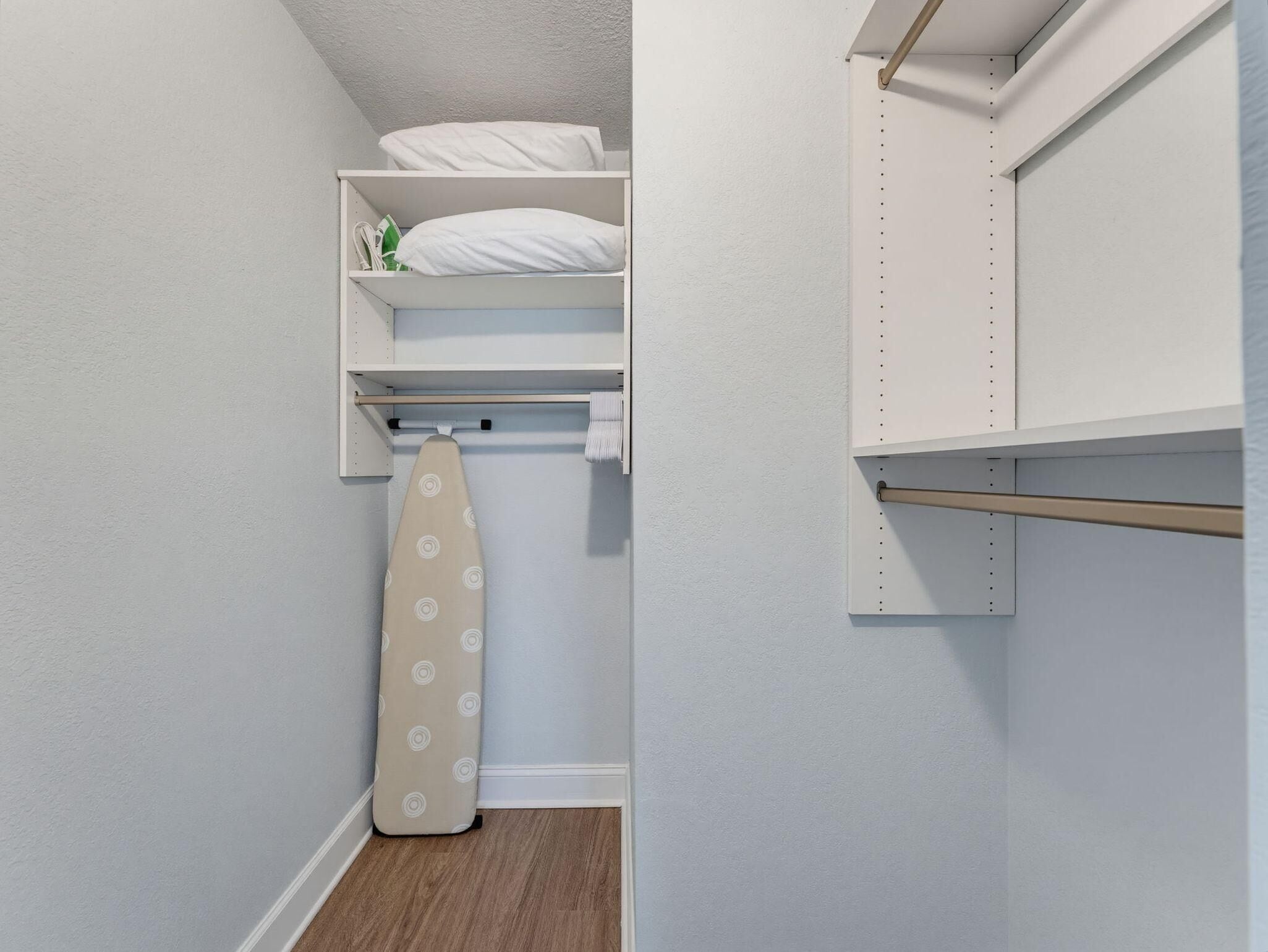Un petit placard bien rangé, doté d’étagères et d’une tringle pour suspendre les vêtements, avec un plancher en bois et une porte sur laquelle est fixé un porte-serviettes.