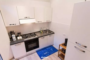 Eine kompakte Küche mit weißen Schränken, einem Gasherd, einem Spülbecken und einer Kaffeemaschine.