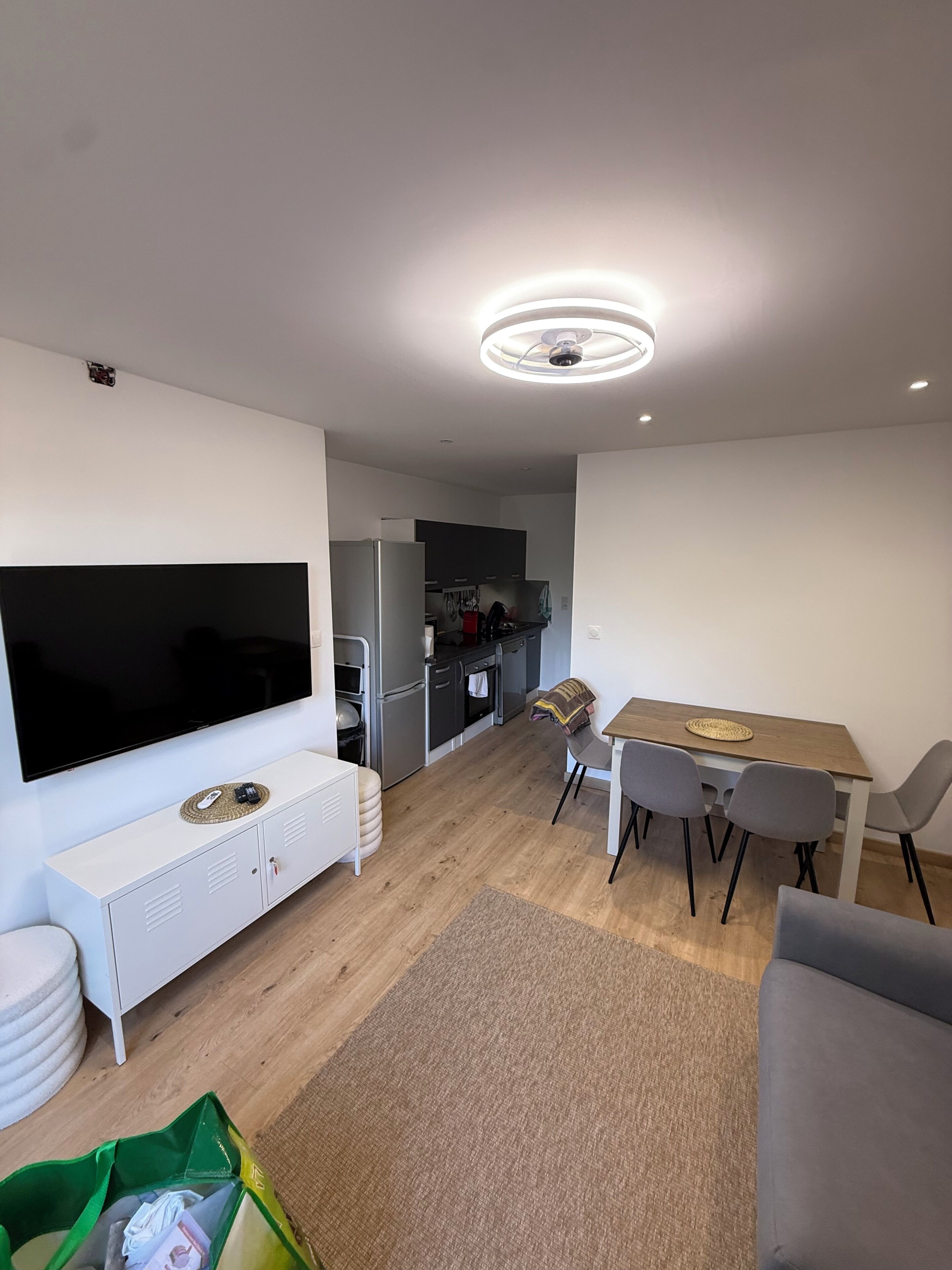 Una sala de estar moderna con un televisor de pantalla plana, un comedor con mesa y sillas, y una cocina al fondo.