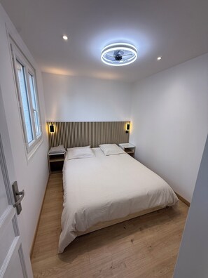 A bedroom with a bed, bedside tables, a wall-mounted light, and a ceiling fan. - Right on the Water: Stunning Apartment in Porticcio (Grosseto-Prugna)