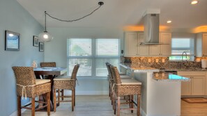 A modern kitchen with a central island, white cabinetry, and a dining area with wicker chairs. - Waterfront, Heated-chilled pool, Outdoor kitchen, downstairs bathroom w/ shower! (cudjoe key)