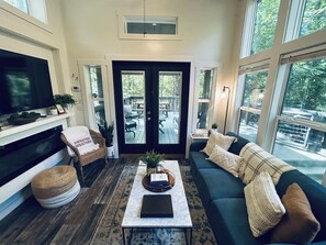 A living room with a fireplace, a television, a sofa, and a coffee table. - Everly House | Waterfall + Private Trails (Monteagle)