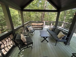 A covered outdoor seating area with a wooden deck, benches, and tables. - Everly House | Waterfall + Private Trails (Monteagle)