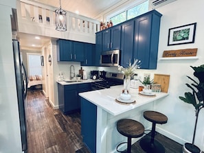A modern kitchen with blue cabinets, a central island with stools, a hanging light fixture, and a sign reading 'Everly House'. - Everly House | Waterfall + Private Trails (Monteagle)