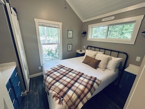 A bedroom with a bed, a window, a bedside table, and a wall-mounted lamp. - Everly House | Waterfall + Private Trails (Monteagle)