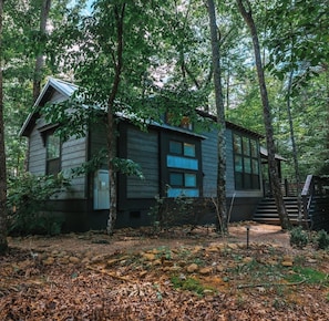 A cabin surrounded by trees with a wooden exterior and a visible staircase leading to the entrance. - Everly House | Waterfall + Private Trails (Monteagle)