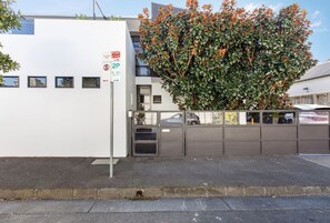 Ein Gebäude mit weißer Fassade, einem verschlossenen Eingang und einem Baum mit grünen und orangefarbenen Blättern.