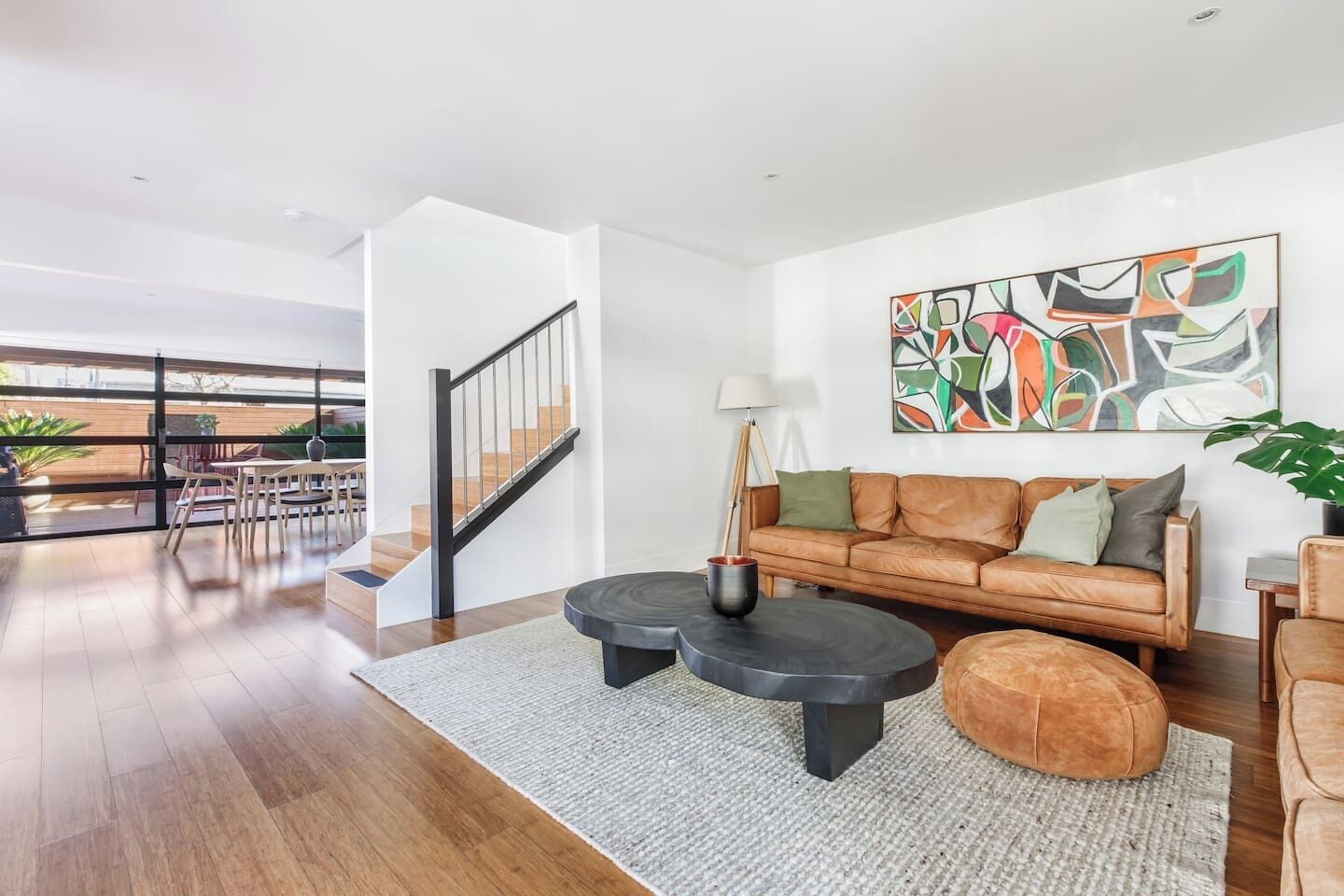 Un salon moderne avec un canapé en cuir, deux tables basses noires et un tableau abstrait aux couleurs vives accroché au mur.