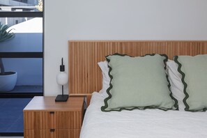 Ein Schlafzimmer mit einem hölzernen Kopfende, einem Nachttisch mit Lampe und Blick auf einen Balkon mit einer Topfpflanze.