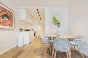 Una cocina moderna con armarios blancos, una isla central y una zona de comedor con una mesa redonda y cuatro sillas grises.