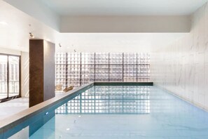 Una piscina con agua cristalina, rodeada por un muro de azulejos y una pared de vidrio.