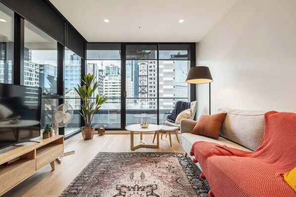 Una sala de estar moderna con un ventanal grande, un sofá, un televisor, un ventilador y una mesa con una planta.