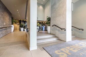 Eine moderne Hotelhalle mit einer Rezeption, einer Treppe und einer Fußmatte mit dem Namen des Hotels.