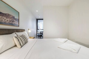 Ein Hotelzimmer mit Bett, Schreibtisch, Stuhl, Lampe und Fenster mit Blick auf Gebäude.