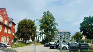 A parking area with cars, a red building, and a modern apartment complex.