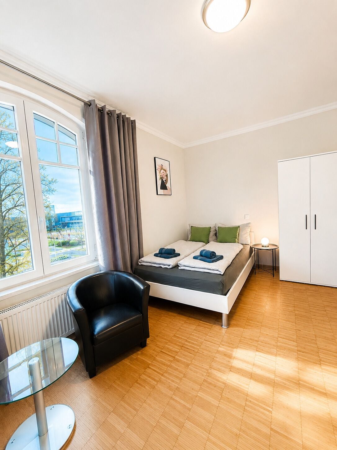Een slaapkamer met een bed, een stoel, een tafeltje, een kast en een raam met gordijnen.