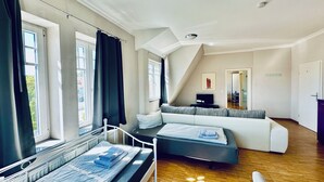 Quarto moderno com cama, sofá, televisão e janela com cortinas.