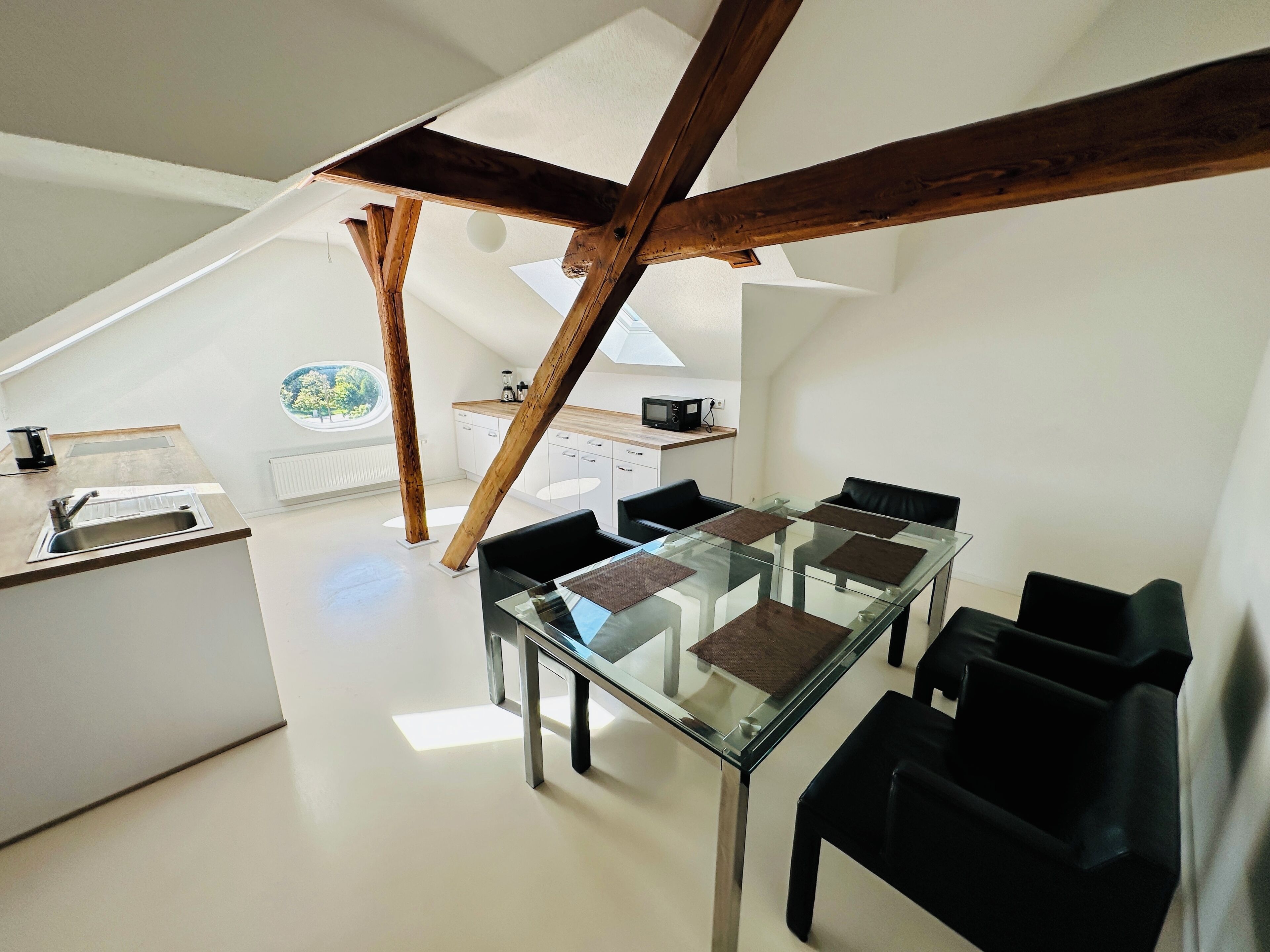 A modern kitchen with a glass dining table, black chairs, and a view of the outdoors.
