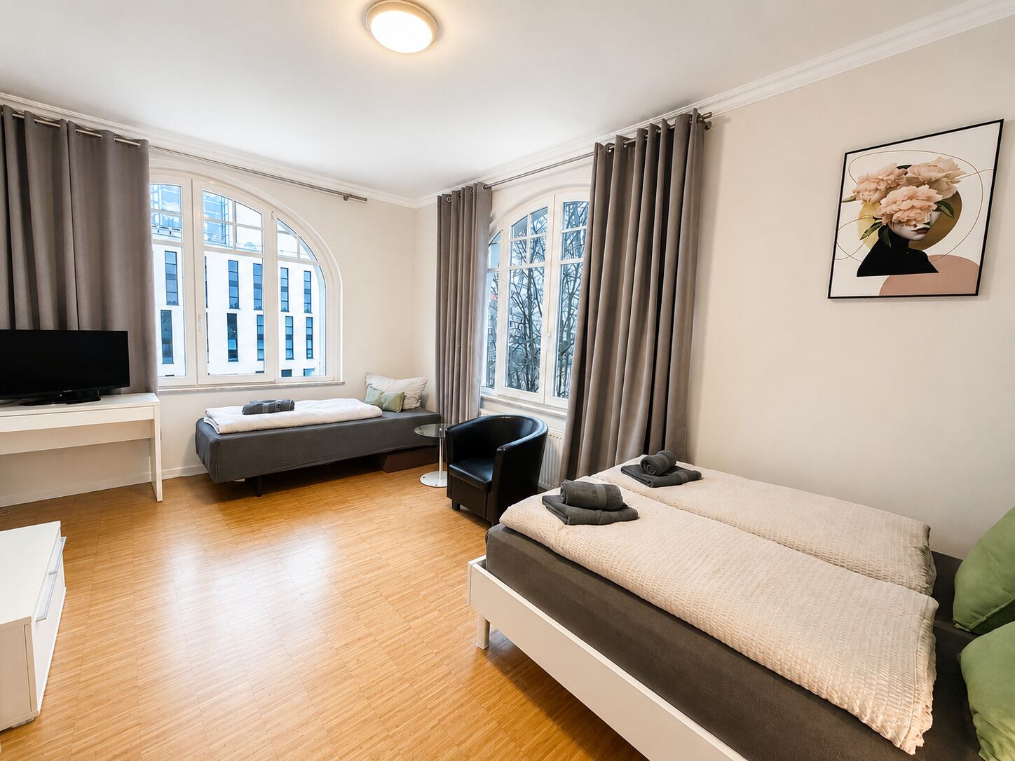 A modern bedroom with a bed, a desk, a chair, and a television.