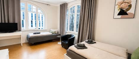 A modern bedroom with a bed, a desk, a chair, and a television.