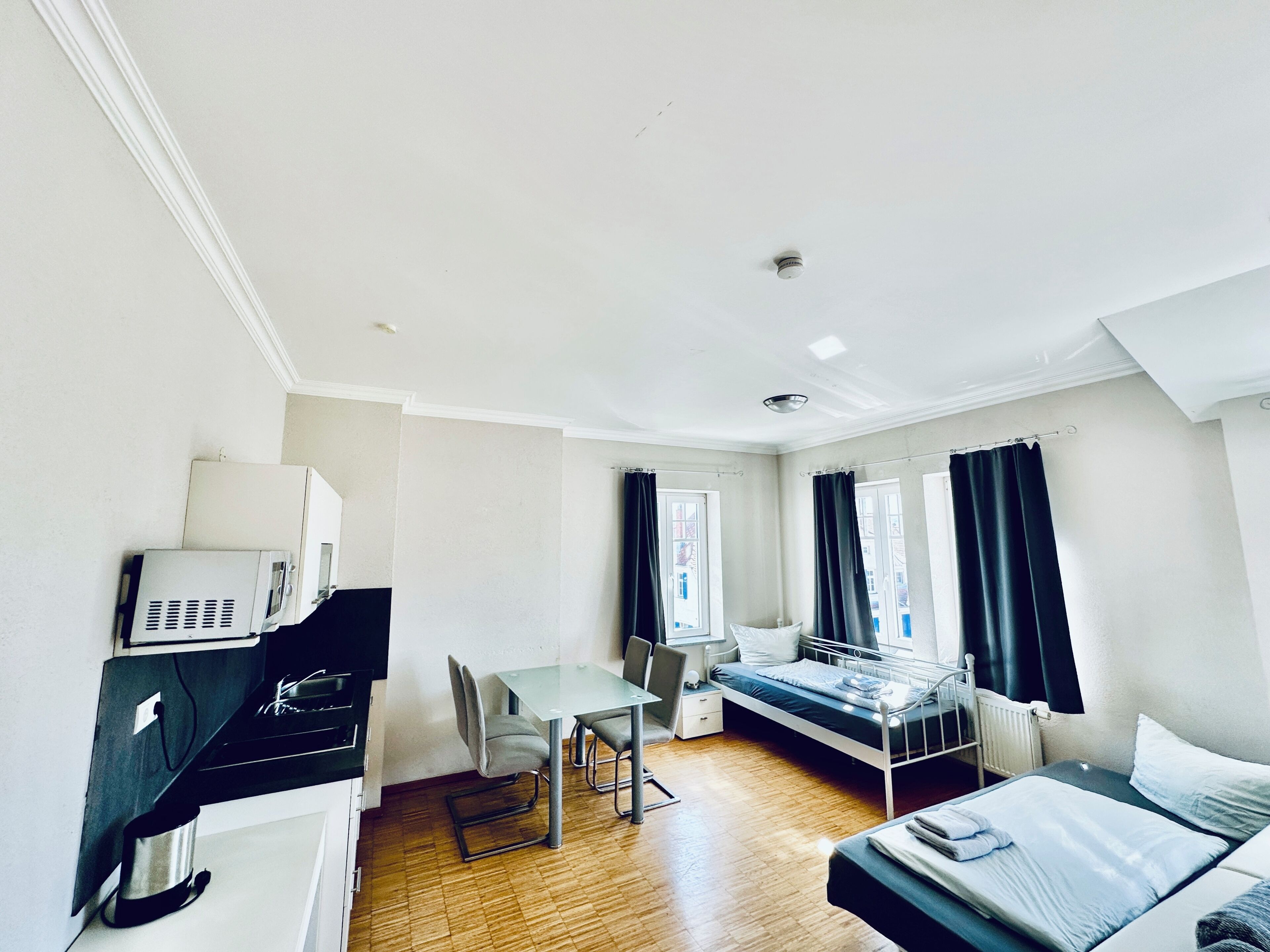 A hotel room with a bed, a desk, a chair, a small table, and a window with curtains.