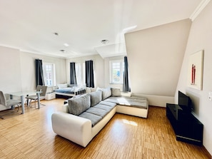 A modern living room with a sectional sofa, a dining table with chairs, a small kitchenette, and a television. - Apartmenthouse Singen  (Singen (Hohentwiel))