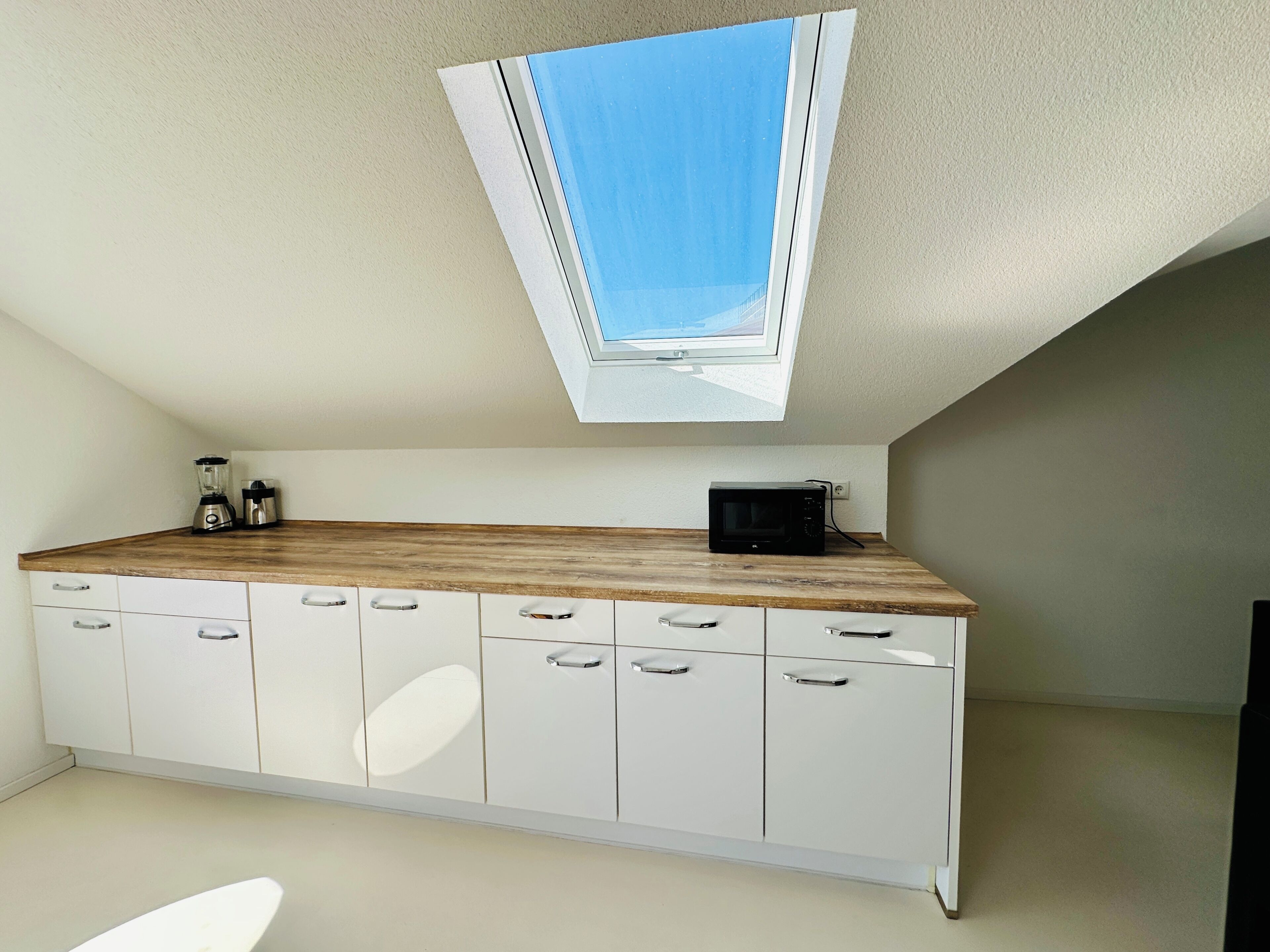 Eine Küche mit Oberlicht, weißen Schränken und einer Holzausziehtafel.