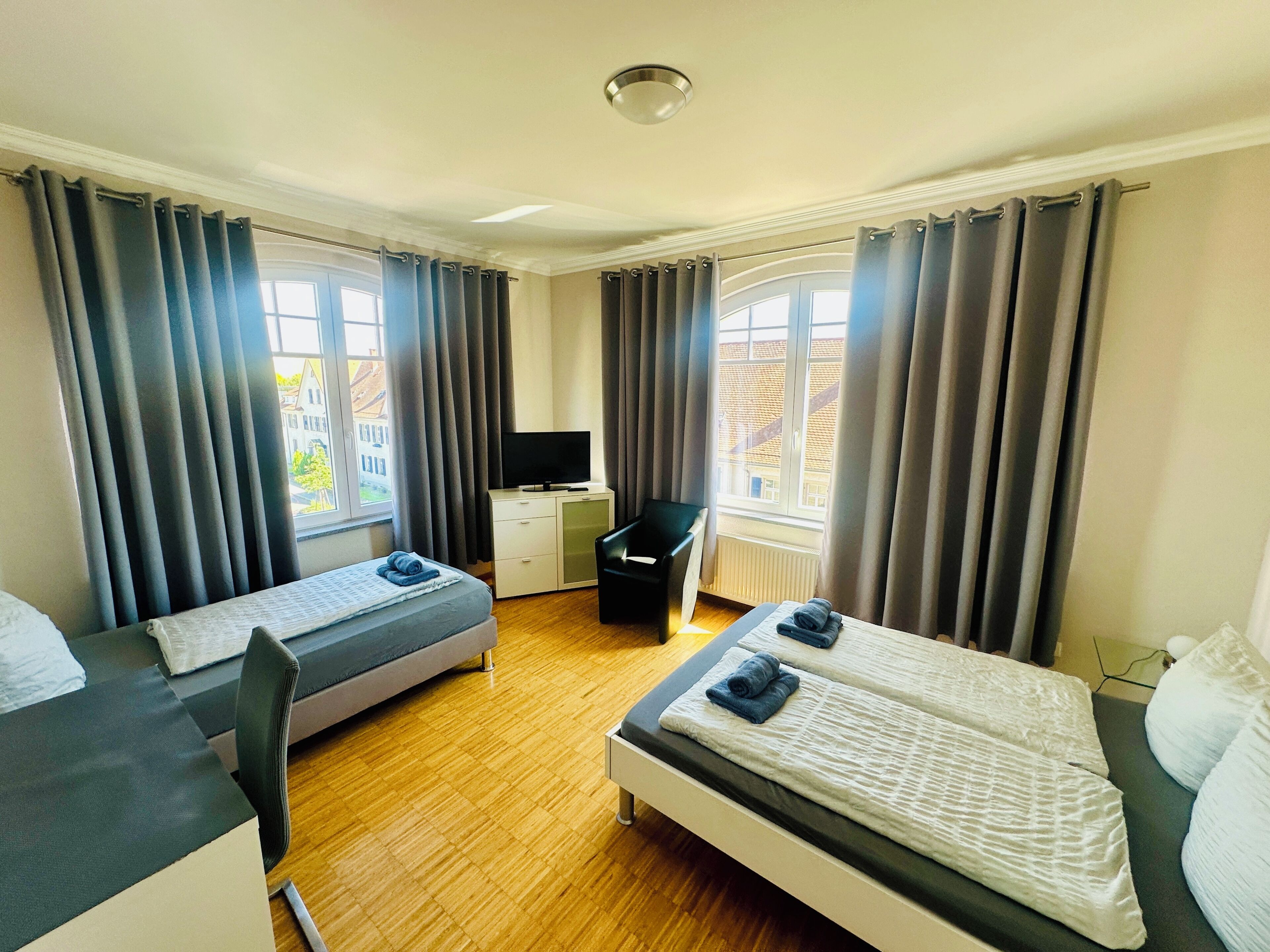 Ein Hotelzimmer mit zwei Betten, einem Schreibtisch, einem Sessel und einem Fernseher.
