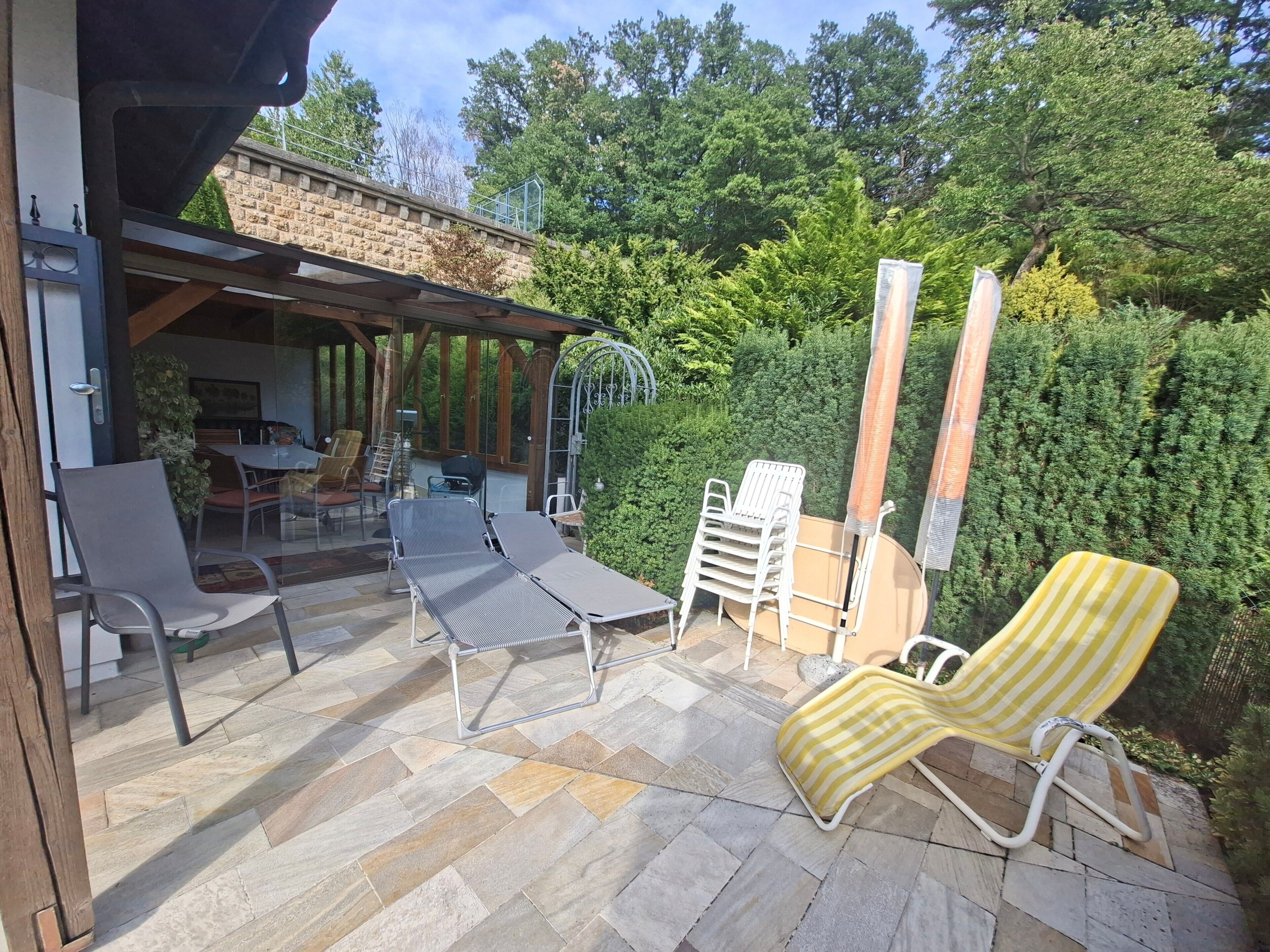 Un patio al aire libre con zona de estar cubierta, suelo de piedra y varios sillones.