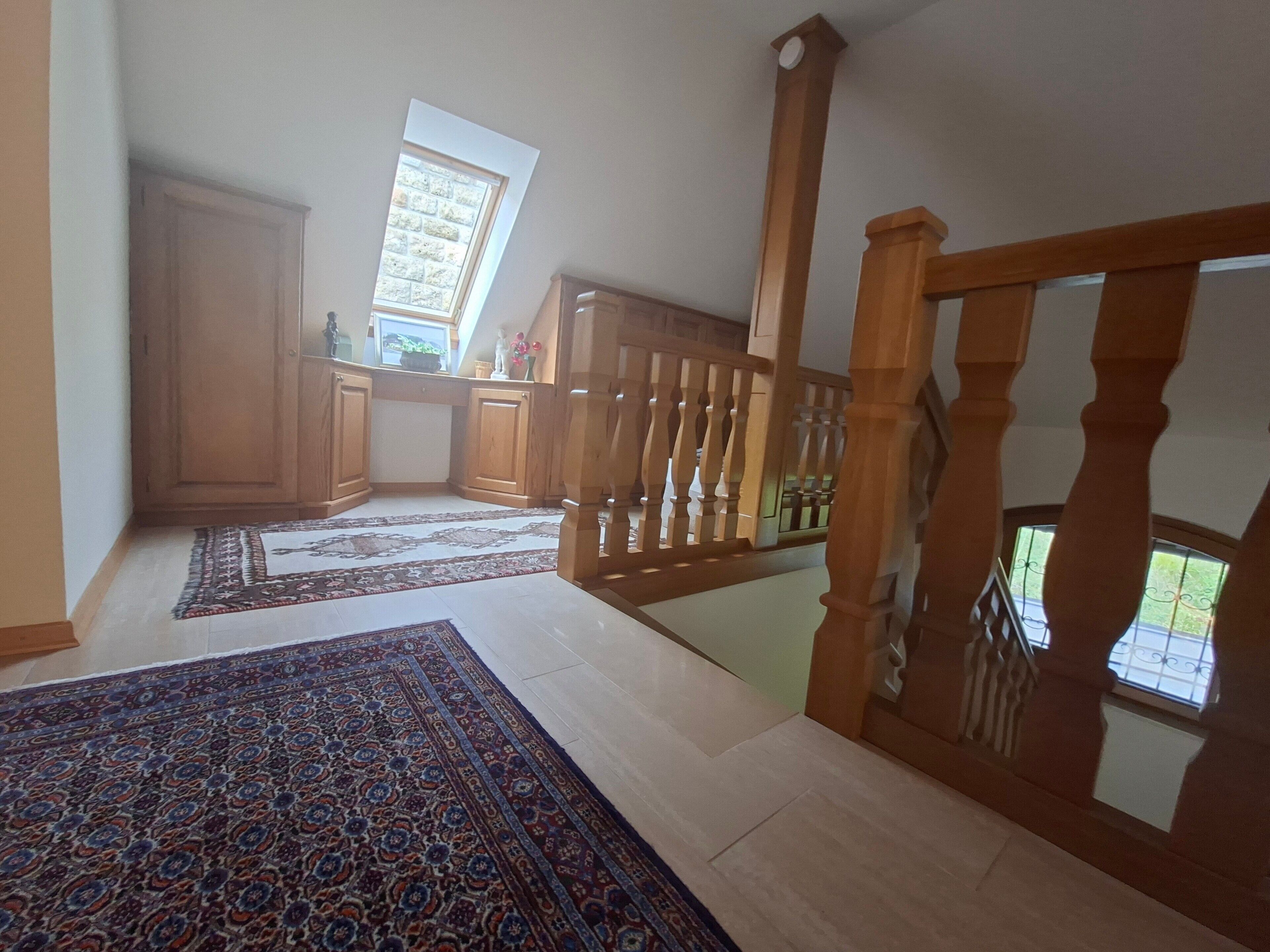 A spacious room with a high ceiling, a wooden staircase, and a view of the outdoors through a window.