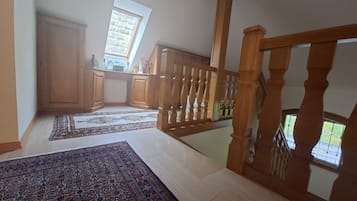 A spacious room with a high ceiling, a wooden staircase, and a view of the outdoors through a window.