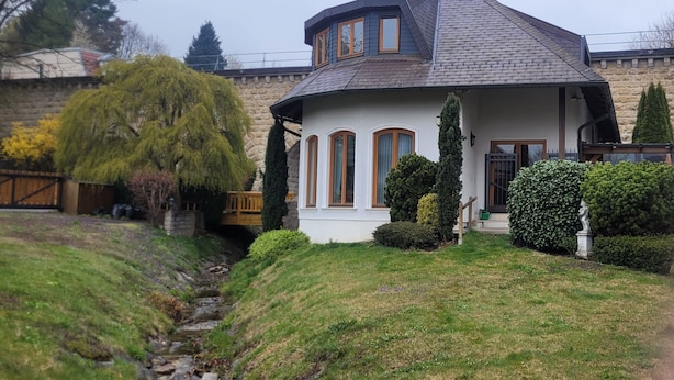 Uma casa com telhado curvo, muro de pedra e um pequeno riacho no quintal.