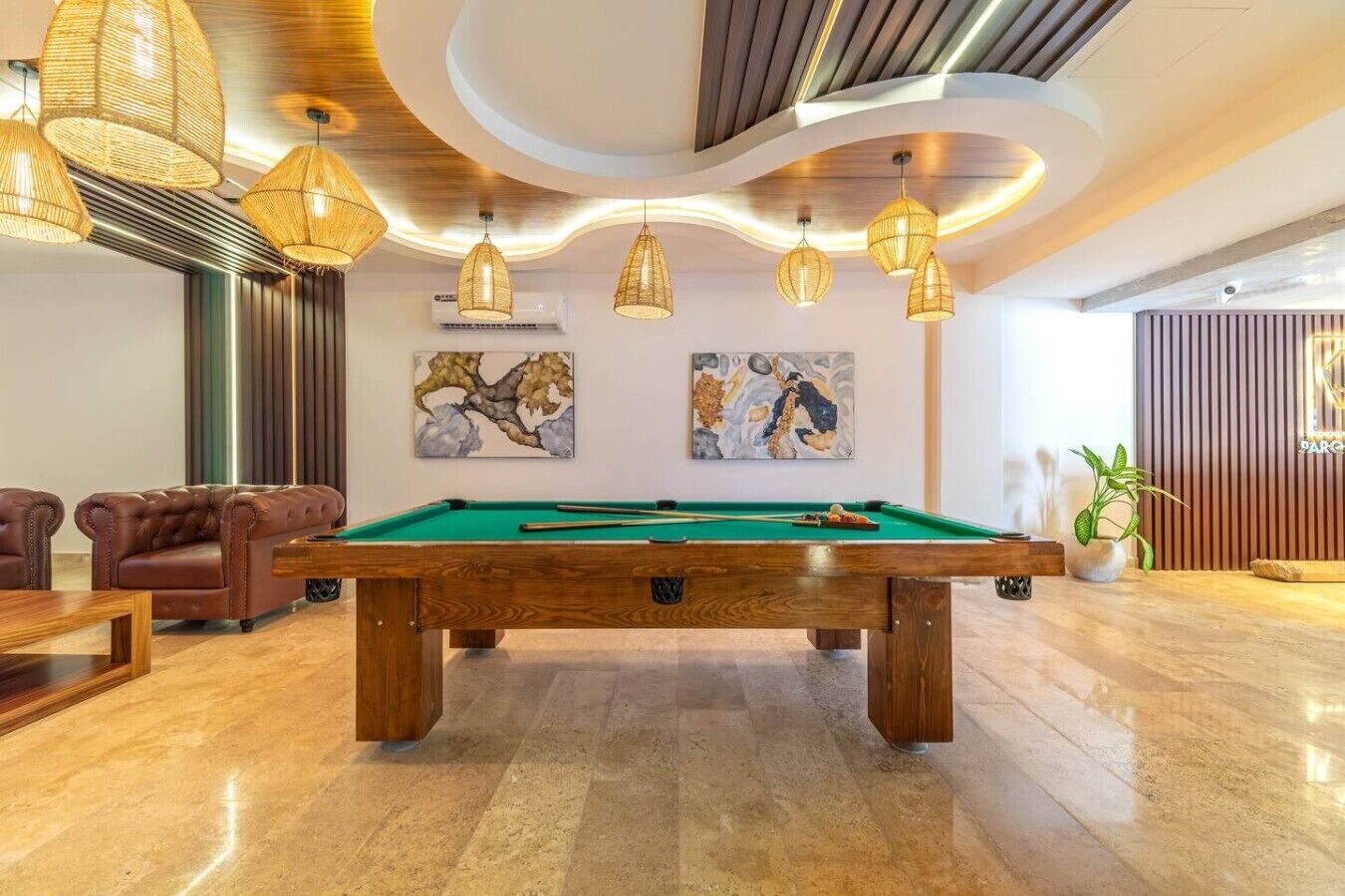Une table de billard dans une pièce dotée d’un plafond voûté, deux tableaux accrochés au mur et une plante en pot.