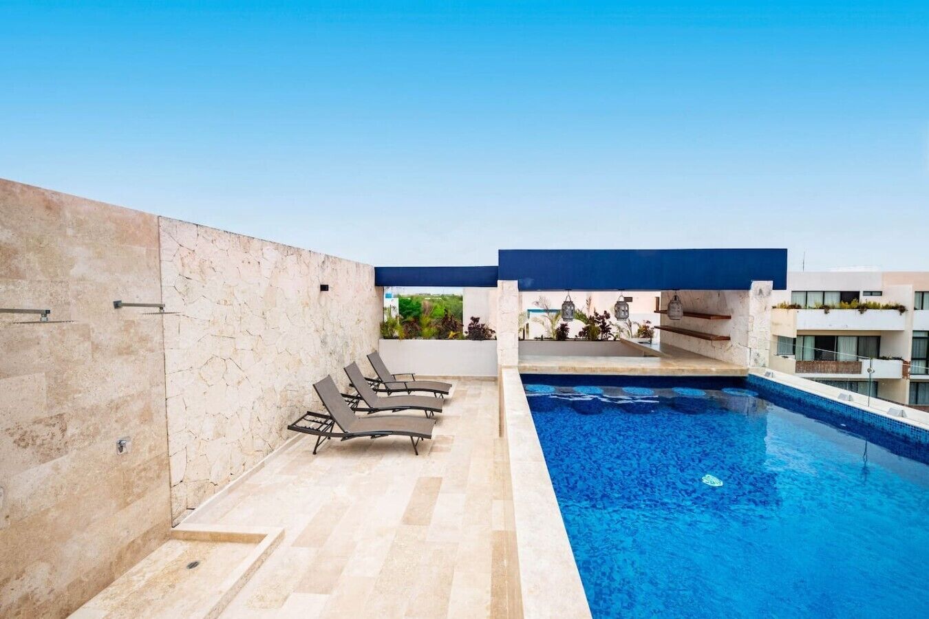 A rooftop swimming pool with lounge chairs and a view of greenery.