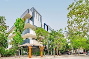 A modern multi-story building with balconies, surrounded by trees and parked cars. - Luxury 2BR | Private Plunge Pool | Rooftop & Gym (Tulum)