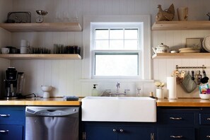 A kitchen with a dishwasher, a sink, and wooden shelves above.