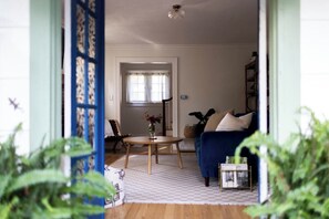 Ett vardagsrum med en blå soffa, ett runt träbord och ett fönster med gardiner.
