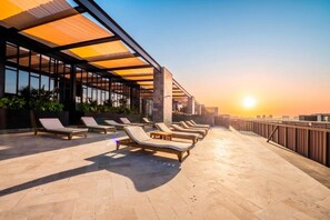 Een terras op het dak met ligbedden en uitzicht op de zonsondergang.