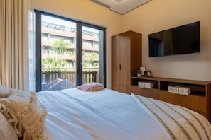 A bedroom with a bed, a TV, a wardrobe, and a balcony with a view of buildings. - Peaceful 1BR Near Beach | Rooftop Pool | Sleeps 4 (Tulum)