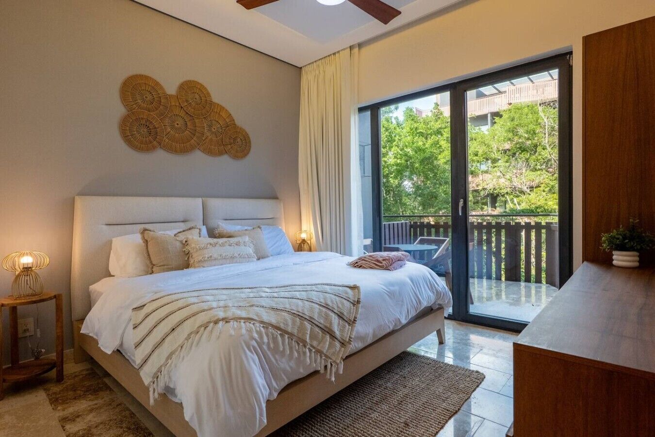 A bedroom with a large bed, a ceiling fan, a wall-mounted decorative piece, and a sliding glass door leading to an outdoor area.