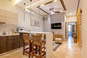 A modern kitchen with a dining area, wooden chairs, a flat-screen TV, and a ceiling fan. - Peaceful 1BR Near Beach | Rooftop Pool | Sleeps 4 (Tulum)