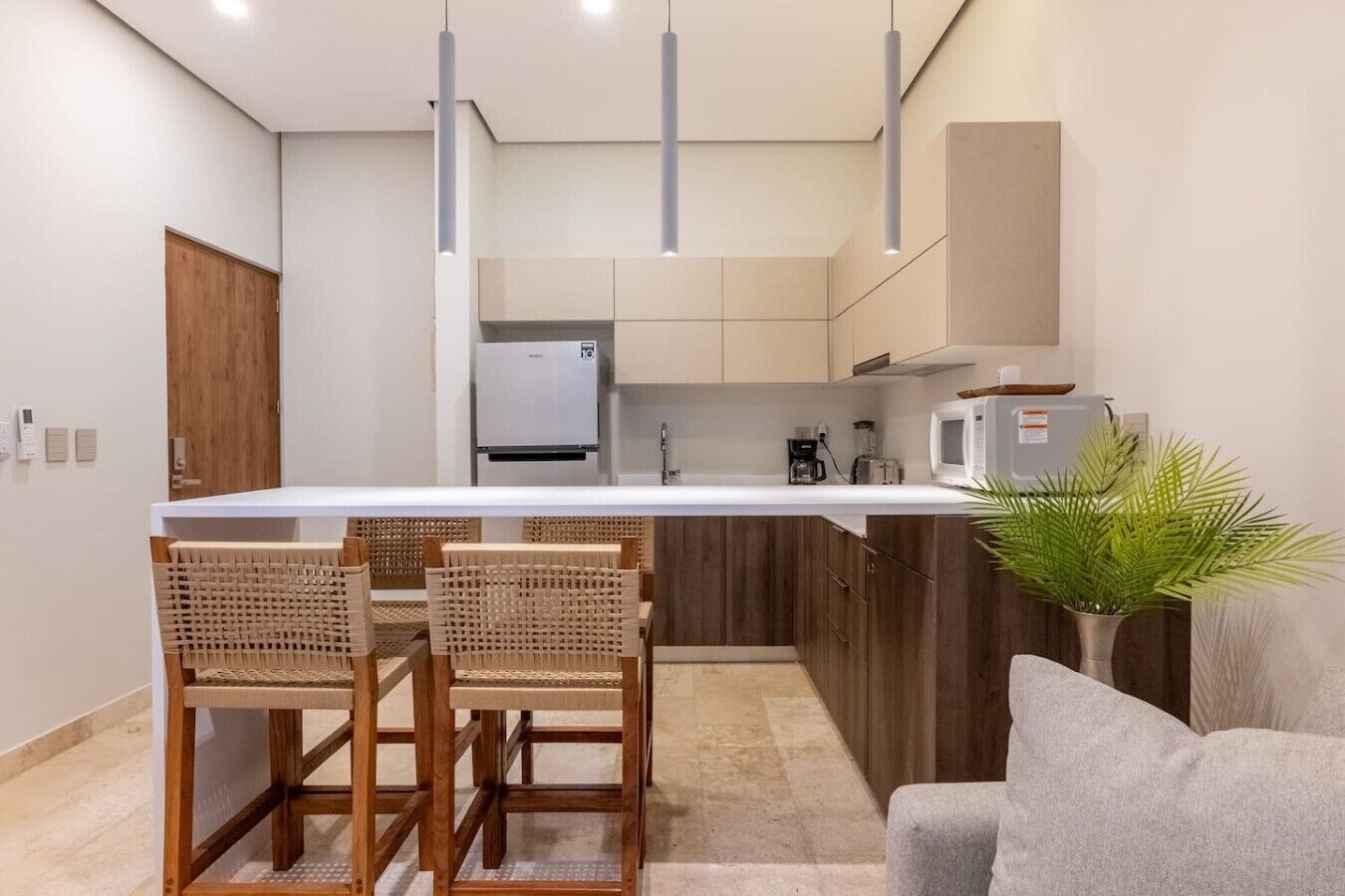 A modern kitchen with a central island, wooden chairs, a grey sofa, and a potted plant.
