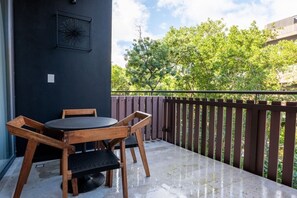 Un balcon avec une table et des chaises en bois, un mur sombre et une vue sur les arbres.